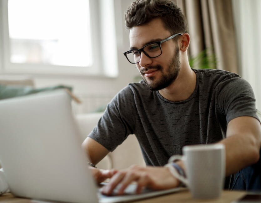 Man with glasses works on a laptop with a cup of coffee next to him