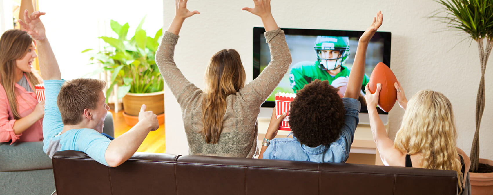Men and women on a couch cheering on a football game on the TV